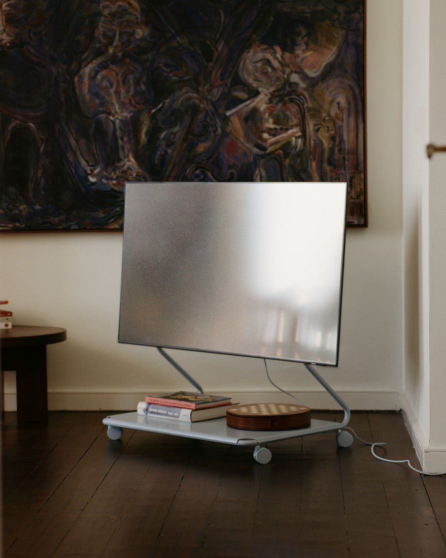 Disco in Powder Blue met tv en wielen in woonkamer, boeken en houten doos op onderplank, schilderij aan de wand