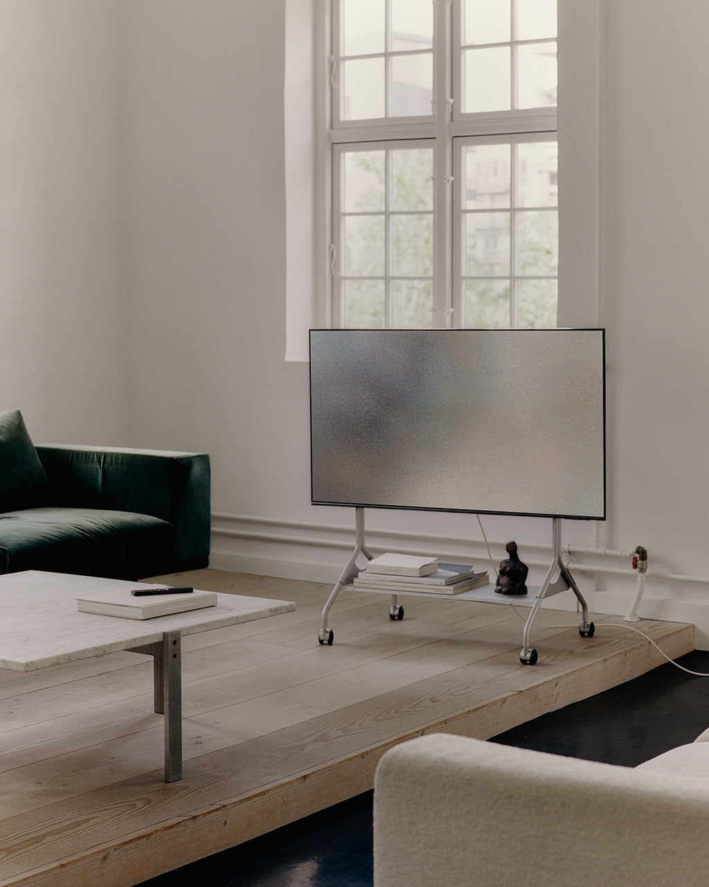 Moon in Cloudy Silver tv-standaard op wielen met tv in lichte woonkamer, op houten podium bij raam, zijaanzicht