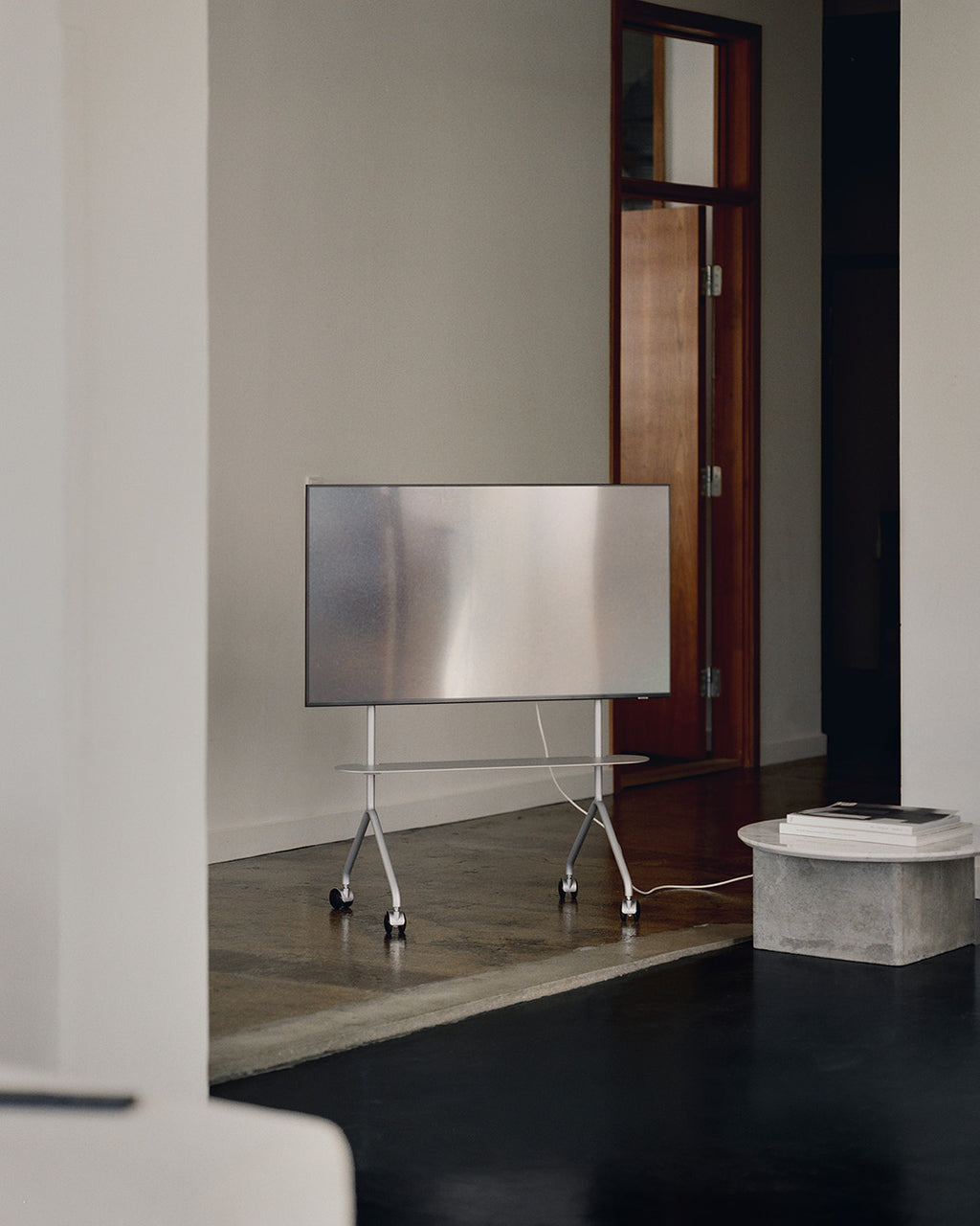 Moon Light in Cloudy Silver tv-standaard op wielen met tv in minimalistisch interieur bij houten deur en betonnen bijzettafel