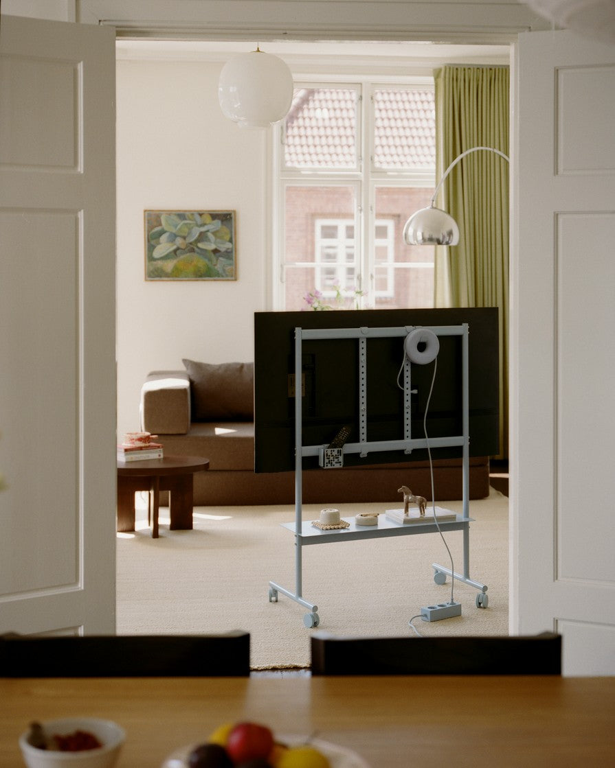 Rover in Powder Blue verrijdbare tv-standaard met gemonteerde tv, achteraanzicht in lichte woonkamer met bank en kunst